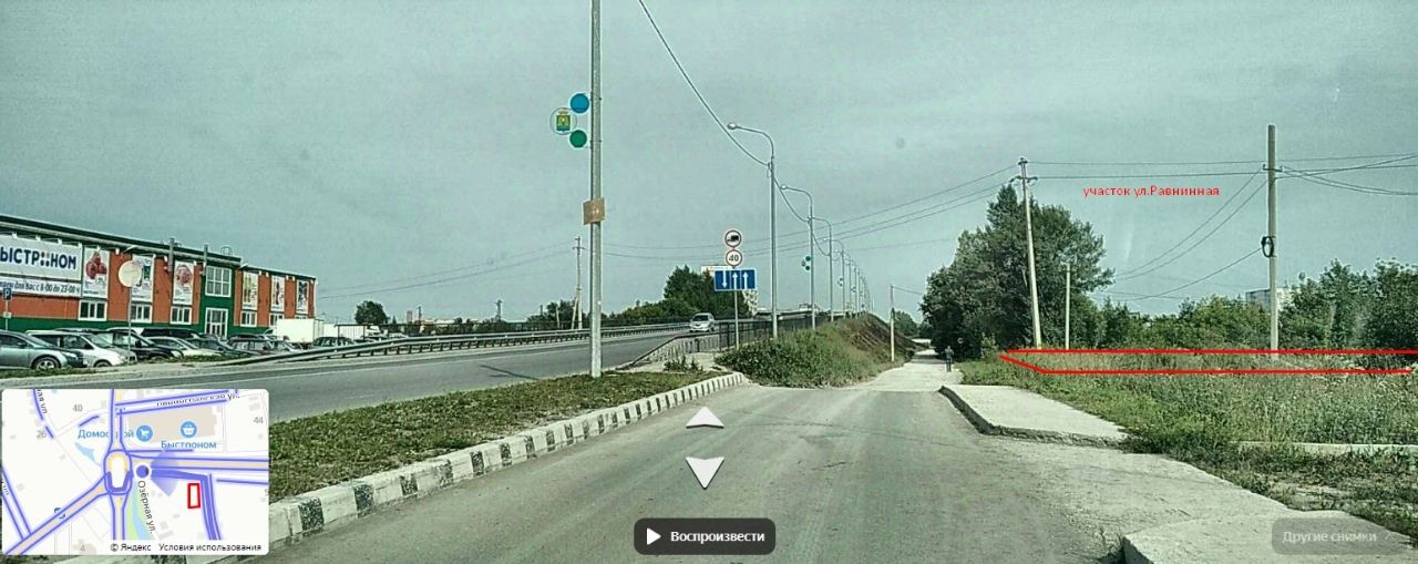 На изображении видна городская улица с асфальтированным покрытием и тротуаром. С одной стороны расположены здания с яркими рекламными вывесками, а с другой – зеленая зона с деревьями и кустарниками. Улица хорошо освещена, с установленными светофорами и дорожными знаками. Видимые материалы включают асфальт, бетонные бордюры и металлические столбы для освещения. Цветовая гамма включает серые и зеленые оттенки, а также яркие цвета рекламы. Пространство выглядит аккуратно и ухоженно, с четкими линиями и организованным движением.