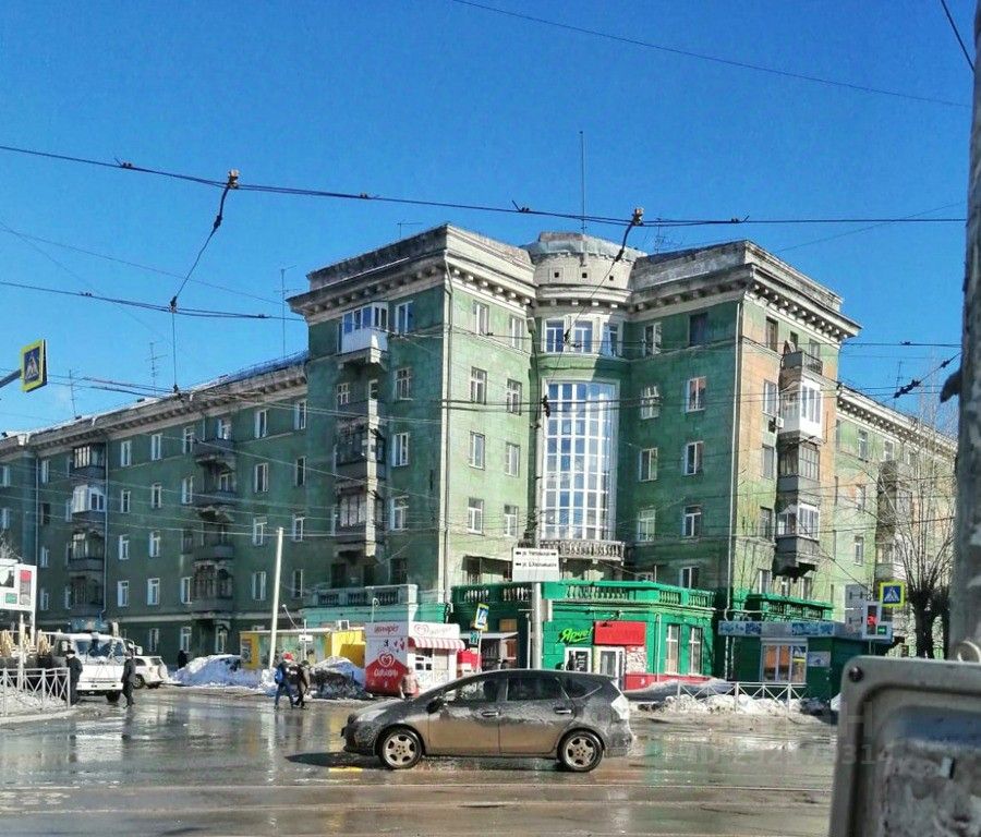 Архитектурный стиль здания характеризуется элементами сталинского ампира с ярко выраженной симметрией и декоративными деталями. Структурные особенности включают балконы с металлическими перилами и большие окна, что создает ощущение пространства. Основная характеристика фасада — зеленая окраска и обилие стеклянных вставок, придающих современный вид. Материалы, используемые в отделке, включают кирпич и стекло, а цветовая гамма варьируется от светло-зеленого до серого, создавая гармоничный контраст. Общий вид здания выражает историческую значимость и функциональность.
