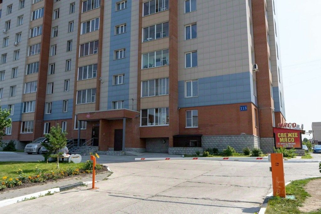 Многоэтажное здание выполнено в современном архитектурном стиле с элементами минимализма. Фасад сочетает в себе кирпичную и панельную отделку, выделяясь контрастными цветами. На первом этаже размещен вход с крышей, а также окна, обеспечивающие естественное освещение. Видны большие окна, которые создают открытое пространство. Цветовая палитра включает серые и коричневые оттенки, что придает зданию современный вид. Входная зона оформлена с использованием каменной отделки, что добавляет прочности и надежности. Пространство вокруг благоустроено с зелеными насаждениями и элементами ландшафтного дизайна.