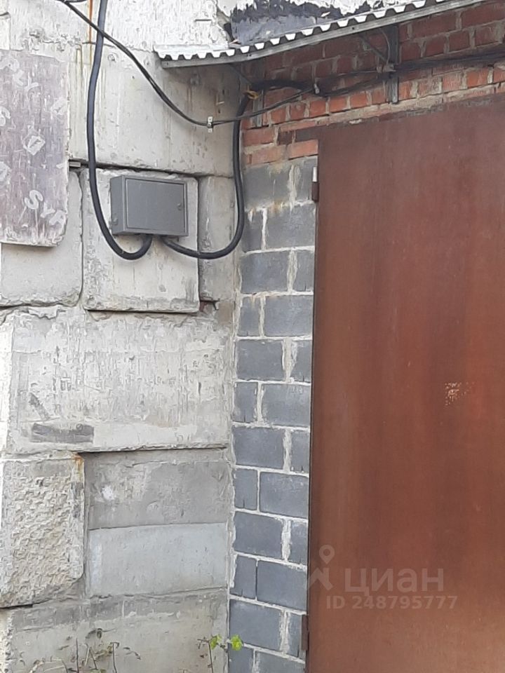 Стена выполнена из кирпича и бетонных блоков, сочетая текстуры и цвета. Видно, что одна часть стены имеет грубую отделку с серыми и светлыми оттенками, а другая — из гладкого коричневого металла, представляющего собой дверь. На стене присутствуют провода, соединяющие электрический щиток, расположенный рядом с дверью. Общий вид создает ощущение функциональности и практичности, характерной для промышленных или хозяйственных помещений.