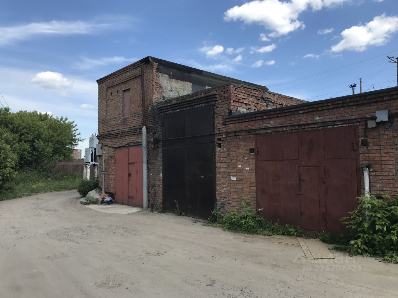 Здание выполнено в индустриальном архитектурном стиле с использованием кирпичной кладки. Видны массивные металлические двери, окрашенные в красный и черный цвета, что придает конструкции строгий вид. Структура имеет простую форму с прямыми линиями, характерными для производственных помещений. Основные характеристики включают прочные стены и отсутствие окон, что указывает на функциональное назначение. Материалы — кирпич и металл, с грубой отделкой, создающей атмосферу утилитарности. Цветовая гамма ограничена черным и красным, что усиливает ощущение надежности и прочности данного здания.