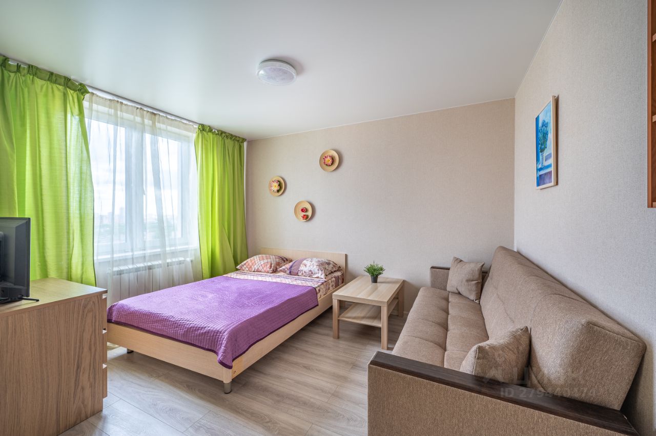 Уютная квартира в Екатеринбурге, 35 кв.м, 1 комната, 30 этаж, без отделки. Просторная гостиная с диваном и кроватью, яркие зеленые шторы.