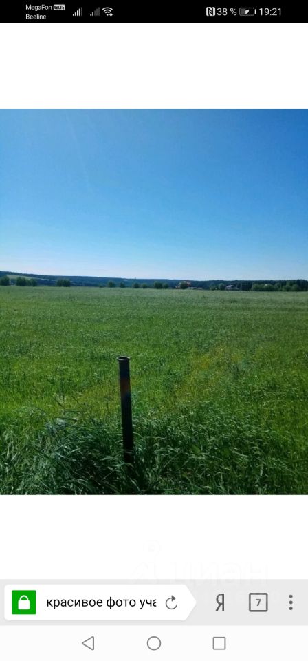 На фотографии представлено открытое пространство, покрытое зелёной травой. Видно, что участок земли ровный и ухоженный, с небольшими участками высокой травы. В центре изображения находится металлический столб, который выделяется на фоне зелёного поля. Небо ясное и голубое, создающее ощущение простора и свободы. Отсутствие построек или других объектов указывает на природный ландшафт. Эта территория может быть использована для различных целей, таких как сельское хозяйство или строительство.