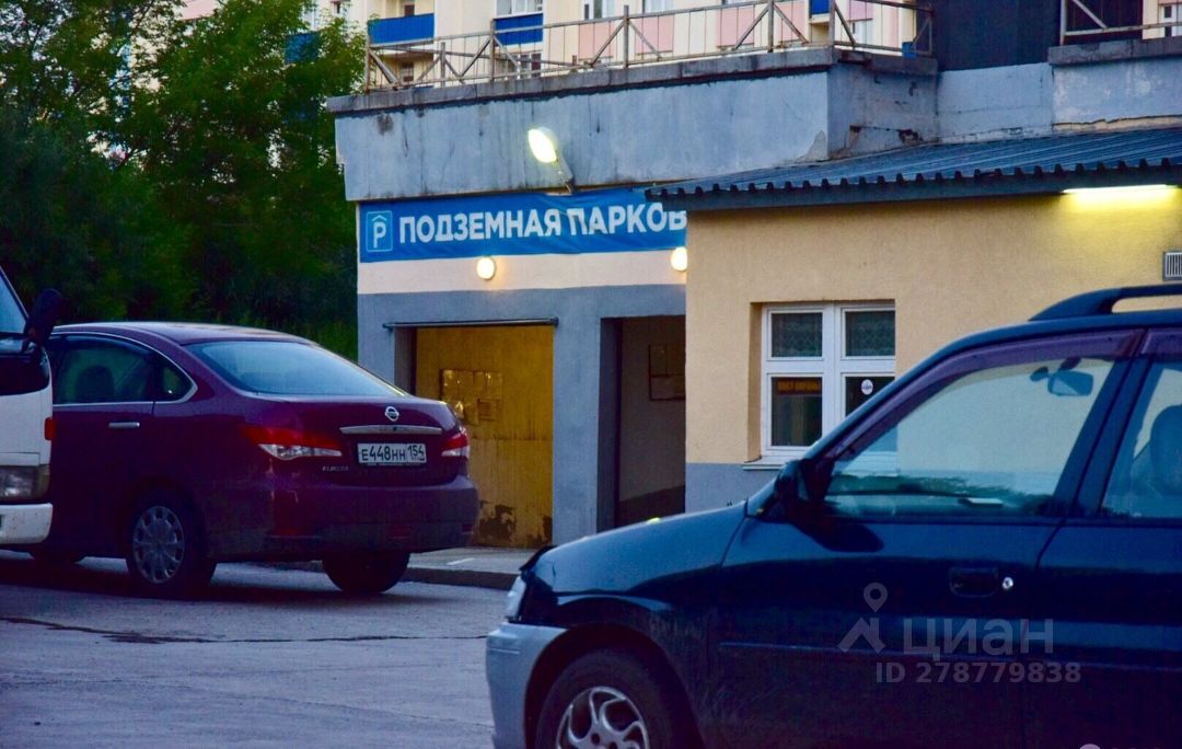 Видна входная зона подземной парковки с яркой вывеской "Подземная парковка". Архитектурный стиль функциональный, с простыми линиями и минималистичным дизайном. Стены окрашены в светло-желтый и серый цвета, что создает контраст. Вход в парковку оформлен широкими дверями, которые обеспечивают легкий доступ. Освещение выполнено с помощью круглых светильников, что добавляет яркости. Рядом припаркованы автомобили, что подчеркивает практическое применение данного пространства. Окна на уровне земли обеспечивают естественное освещение в близлежащих помещениях.