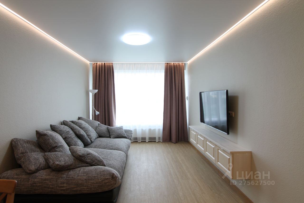 Светлая гостиная с большим окном, уютным диваном и телевизором на стене. Современное освещение и стильный интерьер.