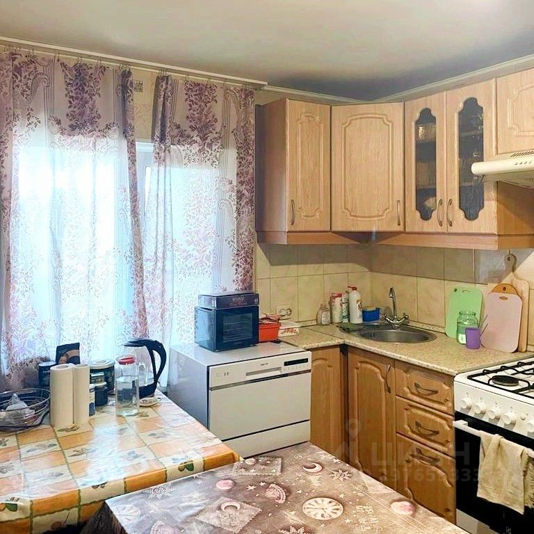 Уютная кухня с современной бытовой техникой и светлыми фасадами. Просторное окно с красивыми шторами. Город: Барнаул.