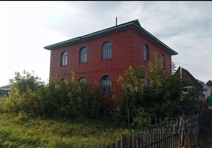 Здание выполнено в традиционном архитектурном стиле с ярко-красным фасадом и характерными арочными окнами. Стены украшены рельефными элементами, придающими конструкции выразительность. Крыша имеет небольшой скат, что добавляет уюта. Видно, что здание окружено зелеными насаждениями, создающими естественный фон. Окна большие, что обеспечивает хорошее освещение внутренних помещений. Используемые материалы выглядят прочными, а цветовая гамма создает теплую атмосферу. Общая композиция здания гармонична и привлекает внимание своим уникальным дизайном.