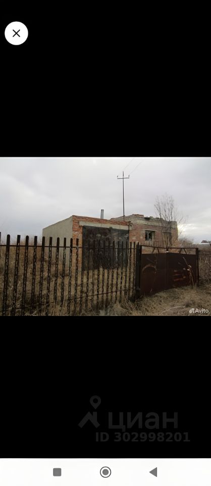 Здание выполнено в простом архитектурном стиле с использованием кирпичной кладки и бетонных стен. Видны незаконченные строительные работы, такие как отсутствие крыши и окон. Структурные элементы включают металлический забор, который окружает участок, и ворота, выполненные из ржавого металла. Основная характеристика пространства — это его незавершенность, что создает ощущение потенциальной возможности для дальнейшей доработки. Цветовая палитра представлена серыми и коричневыми оттенками, а отделка зданий выглядит сырой и неоконченной, что подчеркивает состояние объекта.