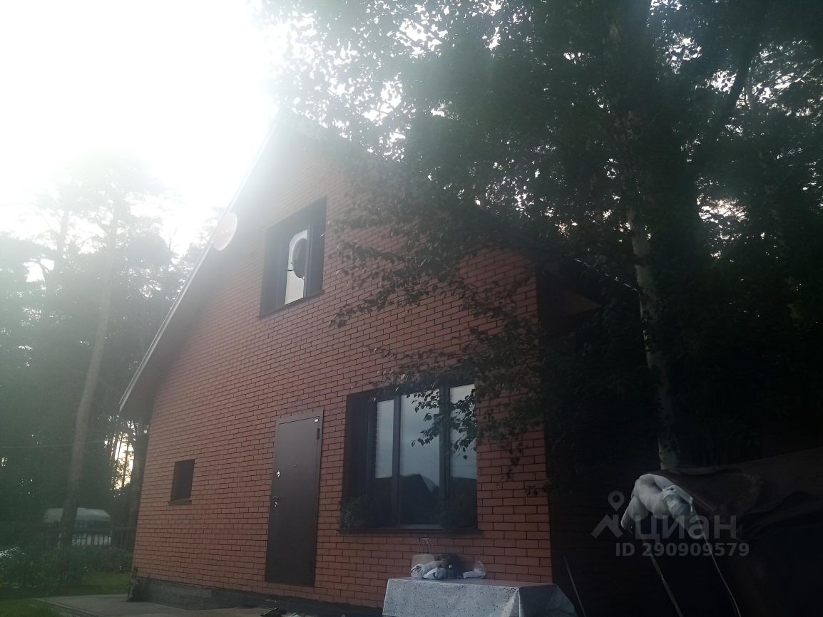 Дом выполнен в современном архитектурном стиле с элементами минимализма. Фасад облицован кирпичом, что придаёт ему прочность и уют. Видны большие окна с темными рамами, обеспечивающие естественное освещение. Основные структурные особенности включают наклонную крышу и входную дверь с современным дизайном. Цветовая палитра теплых оттенков кирпича контрастирует с темными элементами окон и дверей. Пространство вокруг окружено зеленью, что создаёт атмосферу уединения и спокойствия. Основные отделочные материалы включают кирпич и металл, что подчеркивает современный стиль.