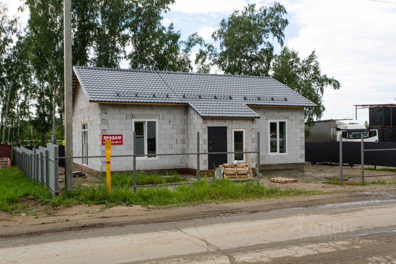 Дом выполнен в современном архитектурном стиле с прямыми линиями и простыми формами. Фасад из белых блоков, крыша покрыта серой металлочерепицей. На переднем плане видны большие окна, обеспечивающие естественное освещение, и центральная дверь. Просторный участок огорожен забором, что придаёт приватность. Использованы нейтральные цвета, создающие гармоничный вид. Основные строительные материалы — бетонные блоки и металл. Открытая планировка предполагает возможность различных вариантов внутреннего обустройства, что позволяет адаптировать пространство под разные нужды.