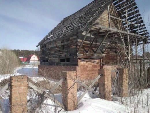 Здание выполнено в традиционном русском стиле с использованием дерева, что придает ему аутентичный вид. Структурные элементы включают наклонную крышу и открытые балки, которые создают ощущение незавершенности. Основная характеристика пространства — это отсутствие окон и обшивка стен, что свидетельствует о запустении. Материалы, использованные в конструкции, преимущественно древесина, с заметными следами старения и разрушения. Цвета натуральные, с преобладанием коричневых и серых оттенков, что подчеркивает атмосферу заброшенности и времени, прошедшего с момента постройки.
