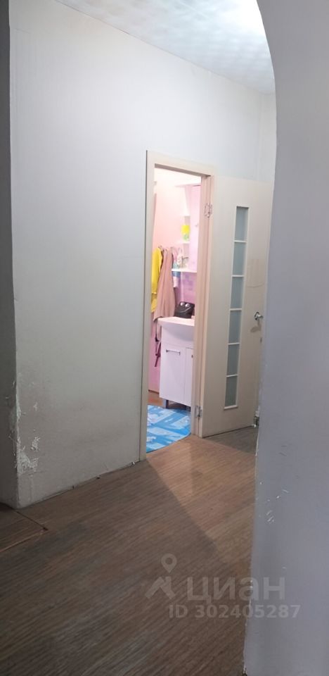 Видна прихожая с простым дизайном и нейтральными цветами. Стены окрашены в белый цвет, пол покрыт ламинатом коричневого оттенка. Дверь с остеклением ведет в помещение, где можно увидеть светлую мебель и элементы интерьера в пастельных тонах. Освещение мягкое, создающее уютную атмосферу. Входная зона оформлена лаконично, без излишних деталей, что подчеркивает функциональность пространства. Общая планировка открыта, что позволяет легко перемещаться между комнатами.