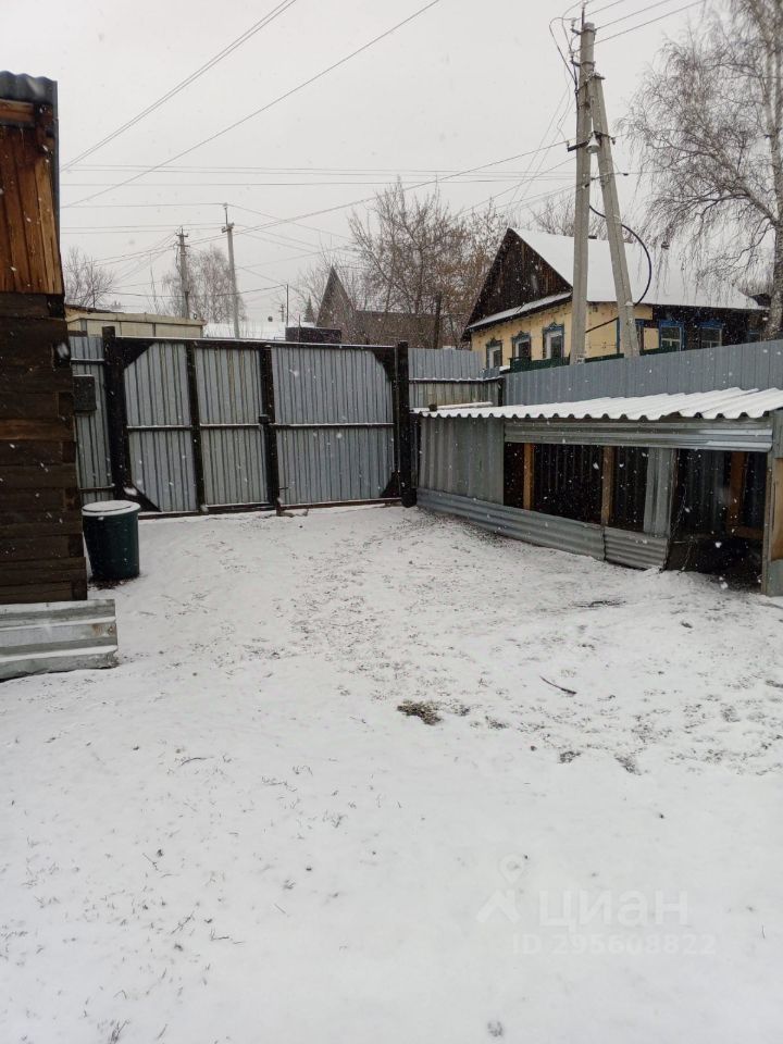 Видно огражденное пространство с металлическим забором, частично покрытым снегом. Пол двора выстлан снегом, на котором видны следы. В углу стоит мусорный бак. Стены соседних построек выполнены из деревянных и металлических материалов, что создает контраст. Пространство выглядит уединенным и защищенным, с минимальным количеством элементов декора. Основные цвета – серый от забора и белый от снега, что придает месту холодный и спокойный вид. Отсутствие мебели и декоративных элементов подчеркивает простоту и функциональность данного участка.