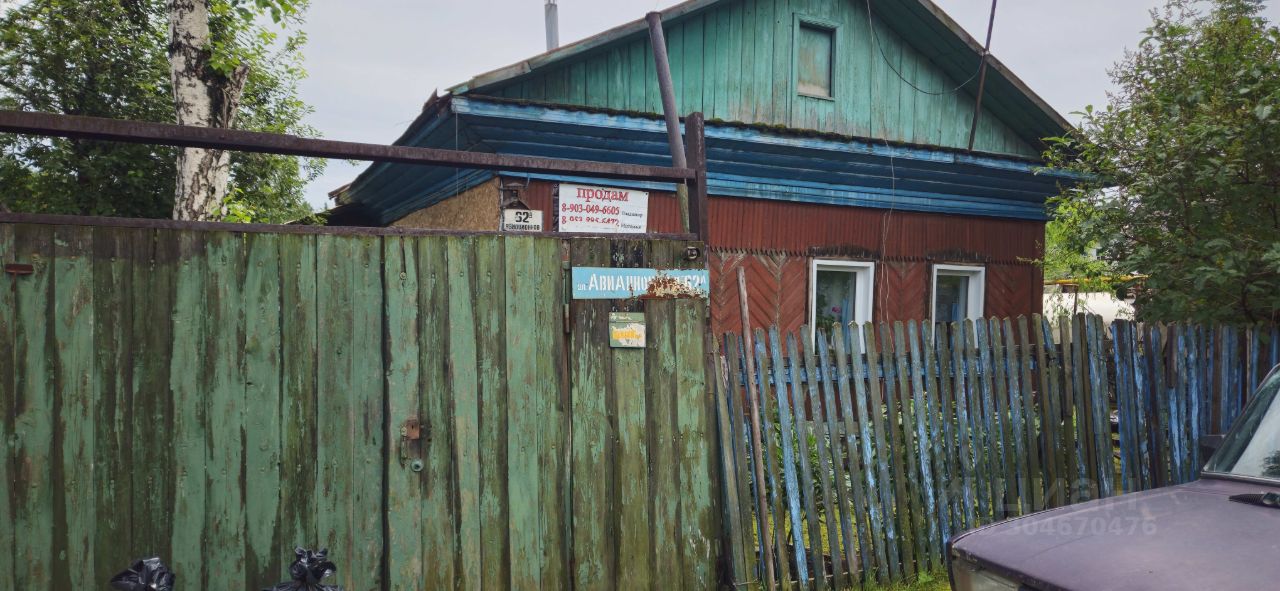 Деревянный дом в народном стиле с яркой крышей и комбинированной отделкой фасада. Стены окрашены в красный и зеленый цвета, что создает контраст. Окна имеют простую форму, обрамленные белыми рамами. Забор выполнен из деревянных досок, окрашенных в различные оттенки синего и зеленого, что придает уникальность. Входная дверь расположена в центре, окруженная элементами декора. Структура выглядит уютно и традиционно, отражая местный архитектурный стиль. Общая атмосфера создает впечатление спокойствия и простоты загородной жизни.