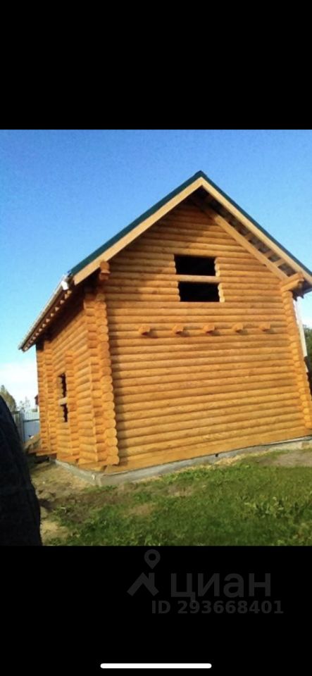 Деревянный дом в стиле бревенчатой постройки с характерными элементами, такими как округлые бревна и крыша с небольшим свесом. Структура имеет симметричную форму и небольшие окна, расположенные на фронтальной стороне. Видимая часть здания показывает чистые линии и натуральный цвет дерева, что придаёт ему уютный и традиционный вид. Отделка выполнена из качественного древесного материала, подчеркивающего экологичность постройки. Крыша покрыта зелёной черепицей, создающей контраст с деревянными стенами и добавляющей визуальную привлекательность.