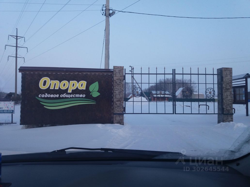 На фотографии виден вход в садовое общество с большими воротами, оформленными в современном стиле. Стена выполнена из бетонных блоков с декоративными элементами, а ворота металлические с узорчатым дизайном. На стене расположена вывеска с названием 'Опора', выполненная в ярких цветах, что придаёт месту привлекательность. Вокруг ворот заметен снежный покров, что создает зимнюю атмосферу. Общий вид подчеркивает уютный и ухоженный характер данного садового общества.