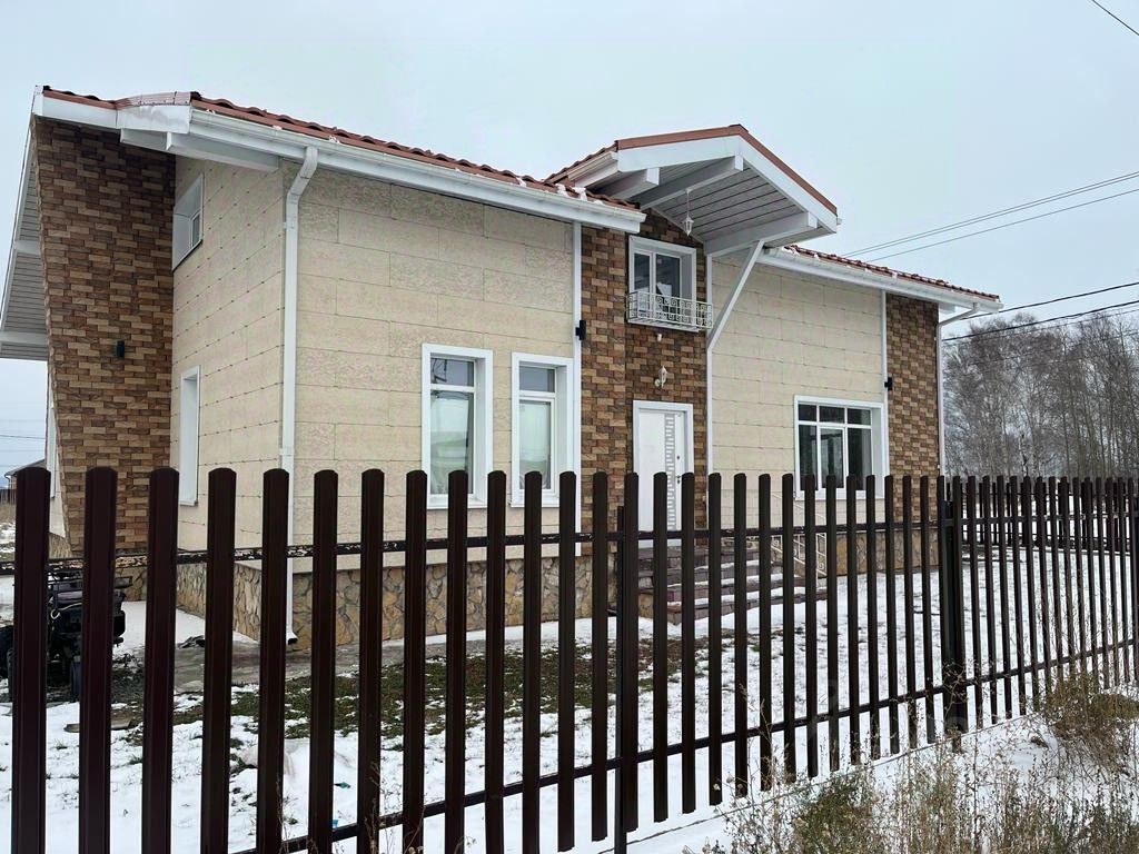 Дом выполнен в современном архитектурном стиле с элементами минимализма. Фасад сочетает светлую штукатурку и коричневый кирпич, создавая контраст. Видны большие окна, обеспечивающие естественное освещение, и крыша с выступами, придающая динамичность. Структура двухэтажная, с балконом на втором этаже и лестницей, ведущей к входной двери. Использованы натуральные материалы, такие как камень и кирпич, что добавляет прочности и эстетики. Цветовая палитра включает нейтральные и теплые оттенки, создавая уютную атмосферу. Общая отделка выглядит аккуратно и современно.