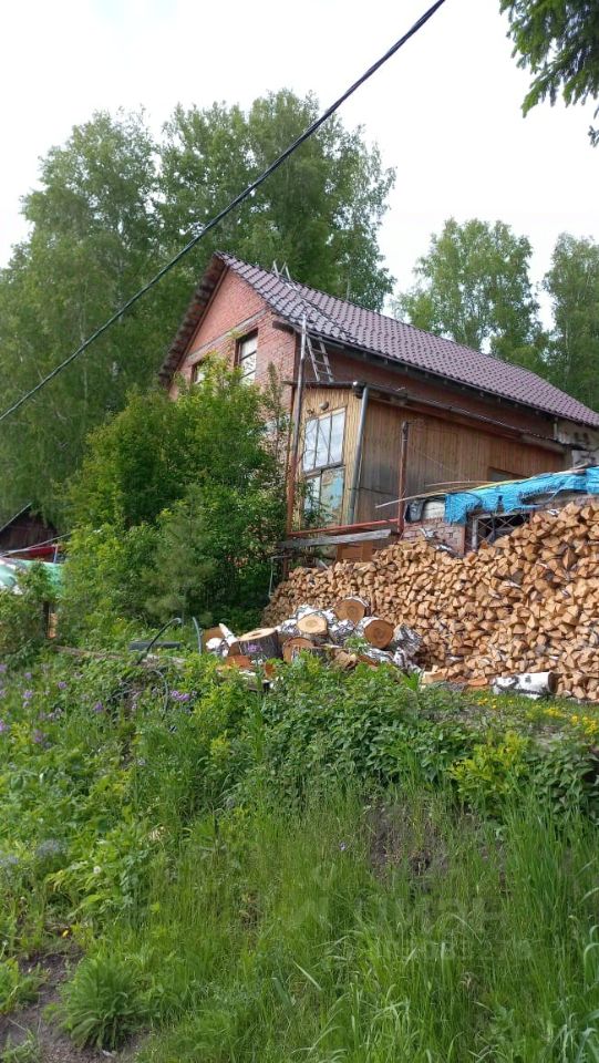 Дом в традиционном русском стиле, построенный из кирпича с деревянными элементами. Крыша двускатная, покрыта черепицей. Видны большие окна, обеспечивающие естественное освещение. Участок окружён зеленью, на котором аккуратно сложены дрова. Основные цветовые акценты — красный кирпич и коричневое дерево. Стены частично обшиты деревом, что придаёт уютный вид. Функциональная планировка предполагает наличие нескольких зон, включая место для хранения дров. Общая атмосфера — гармония с природой и традиционное русское жилище.