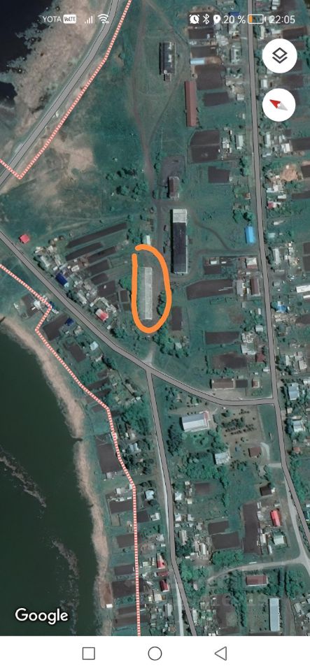 На изображении виден участок земли с несколькими строениями, расположенными вдоль дороги. Архитектурный стиль зданий варьируется, с простыми прямыми линиями и крышами из металлочерепицы. Структурные особенности включают одноэтажные и многоэтажные здания, некоторые из которых имеют большие окна. Основные характеристики помещений не видны, однако можно предположить наличие складских или производственных пространств. Цвета фасадов зданий преимущественно нейтральные, с элементами ярких оттенков на крышах. Материалы, вероятно, включают бетон и металл, что подчеркивает функциональность объектов.