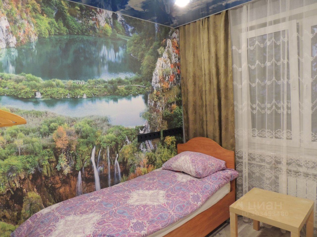 Уютная комната с живописными обоями, односпальная кровать, окно с занавесками, столик. Идеально для комфортного проживания в Екатеринбурге.