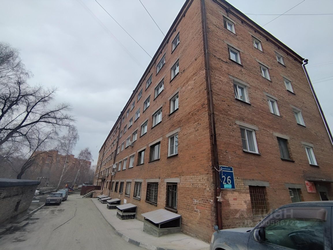Здание выполнено в стиле советской архитектуры с характерным кирпичным фасадом. Видны большие окна с металлическими рамами, а также выступающие элементы, такие как подоконники. Структура имеет три этажа, с симметричным расположением окон. Входная зона оформлена с использованием каменных ступеней и небольших площадок. Основные материалы – красный кирпич и бетон. Цветовая гамма нейтральная, с преобладанием красного и серого тонов. Завершает облик здания крыша с небольшим наклоном, что подчеркивает его функциональность и простоту.