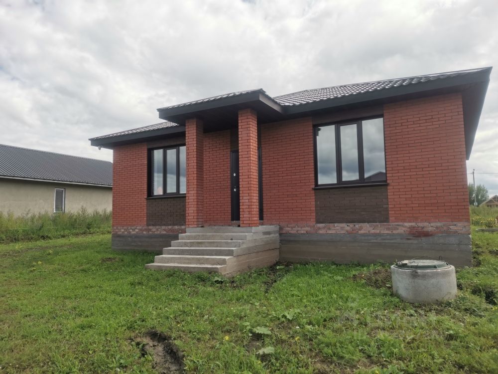 Фасад дома выполнен в современном архитектурном стиле с использованием кирпичной кладки. Основные элементы дизайна включают большие окна, которые обеспечивают естественное освещение, и симметричную компоновку. Ступени ведут к входной двери, подчеркивая функциональность и доступность. Цветовая гамма состоит из теплых кирпичных тонов, что создает уютную атмосферу. Использование качественных материалов, таких как кирпич и бетон, придает зданию прочность и долговечность. Крыша с наклоном добавляет динамичности и защищает от атмосферных воздействий, что делает дом привлекательным и практичным.