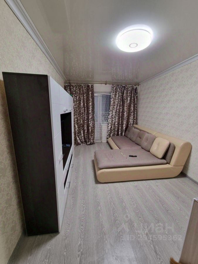 Светлая гостиная с современной мебелью, уютный диван, стильный шкаф, большие окна с плотными шторами. Идеально для комфортного проживания.