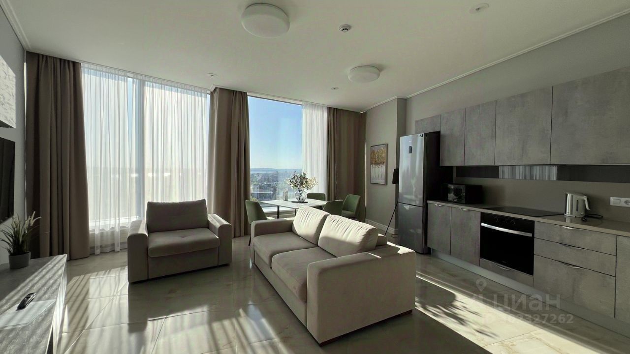 Светлая квартира на 24 этаже в Екатеринбурге, просторная гостиная с большими окнами и современной кухней, 82 кв.м, 2 комнаты