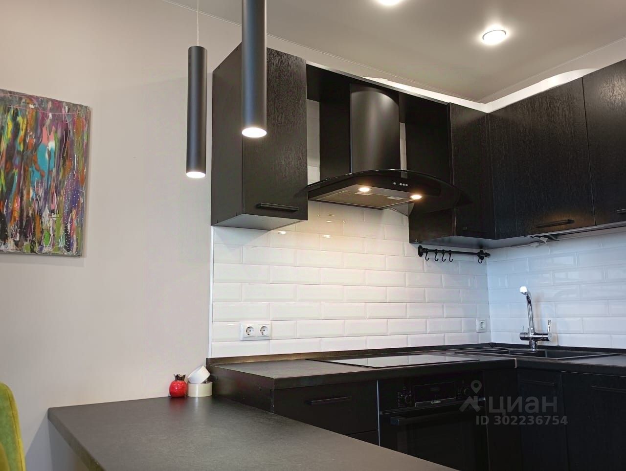 Современная кухня с черными шкафами и белой плиткой, стильное освещение, картина на стене. Квартира на 14 этаже в Екатеринбурге.