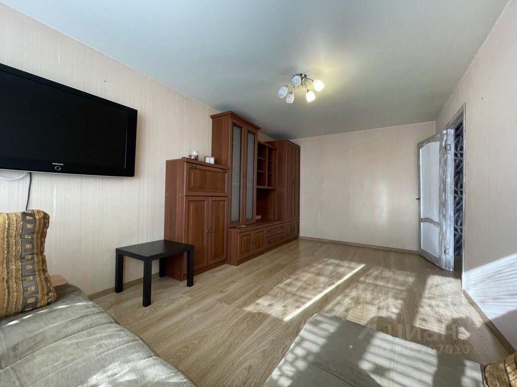 Уютная однокомнатная квартира на первом этаже в Екатеринбурге. Просторная комната с мебелью и телевизором, светлый интерьер.