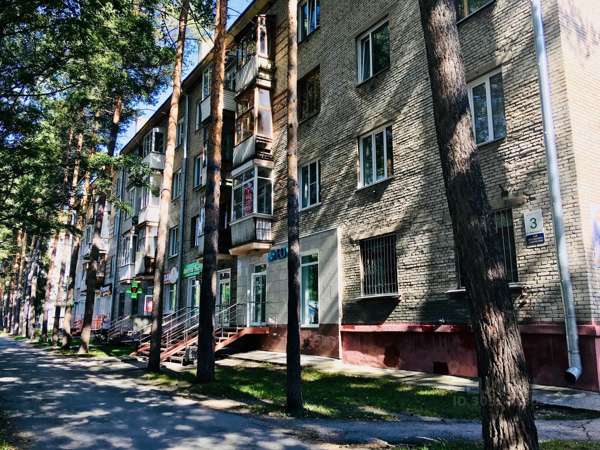 Здание оформлено в стиле советской архитектуры, с характерными кирпичными стенами и простыми геометрическими формами. Видны балконы с металлическими перилами и большие окна, обеспечивающие естественное освещение. На первом этаже расположены коммерческие помещения с витринами, оформленными в современном стиле. Цветовая палитра включает светло-серые и бежевые оттенки, а отделка стен выполнена из кирпича с минималистичным дизайном. Удобные металлические лестницы ведут к входам, подчеркивая функциональность здания.