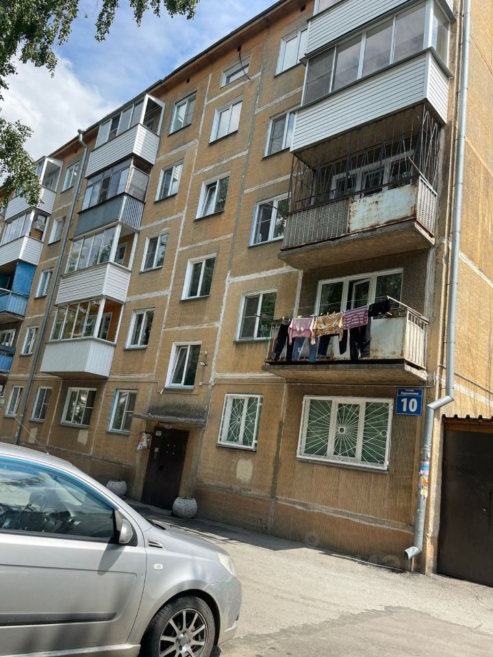 Здание выполнено в советском архитектурном стиле, характеризуется простыми геометрическими формами и функциональностью. Фасад отделан желтым кирпичом с явными следами износа. Видны большие окна с металлическими решетками, которые обеспечивают безопасность. На балконах размещены сушащиеся вещи, что добавляет уют и атмосферу жизни. Основные цвета фасада — желтый и серый, а также элементы из металла. Структура включает несколько этажей, с балконами, которые выступают из общей линии фасада, создавая интересный визуальный эффект.