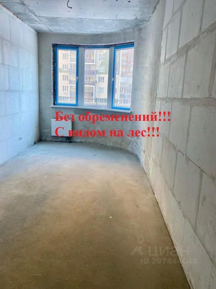 Помещение с округлыми углами и большими окнами, оформленными в голубом цвете. Стены выполнены из бетонных блоков, что придаёт интерьеру современный вид. Полы гладкие, без покрытия, что создаёт ощущение открытого пространства. Окна обеспечивают естественное освещение и панорамный вид, что делает комнату светлой и просторной. Отсутствие отделки позволяет будущему владельцу самостоятельно выбрать стиль и материалы. Основные характеристики включают в себя возможность организации различных функциональных зон благодаря гибкому планированию.