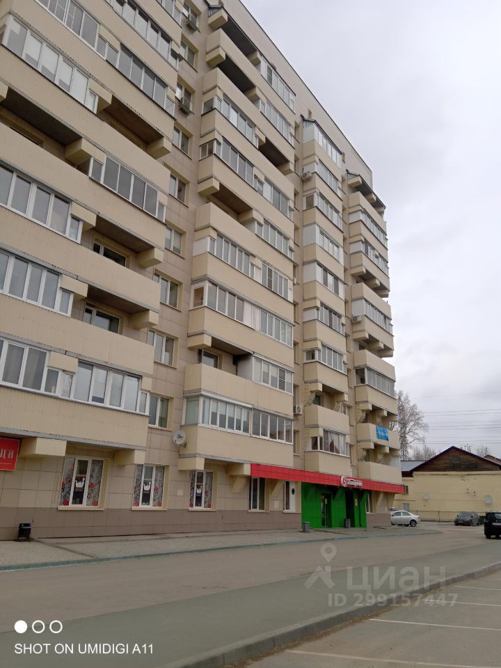 Здание выполнено в современном архитектурном стиле с элементами минимализма. Видны балконы с остеклением, что придаёт фасаду лёгкость и открытость. Структурно здание имеет несколько этажей, с симметрично расположенными окнами. На первом этаже расположены коммерческие площади с яркими вывесками. Основные отделочные материалы — светлый кирпич и панельные элементы, что создаёт гармоничное сочетание. Цветовая гамма фасада включает бежевые и серые оттенки, а также яркие акценты в виде красного и зелёного на первых этажах. Общий вид здания выглядит современно и привлекательно.