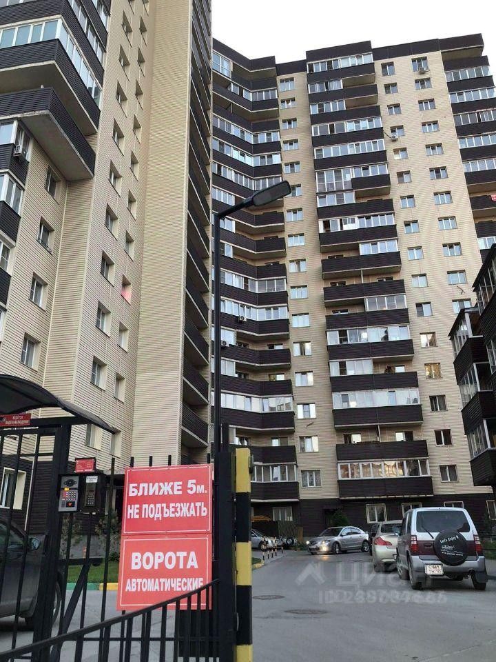 Здание выполнено в современном архитектурном стиле с элементами минимализма. Фасад сочетает светлые и темные панели, создавая контраст. Видны балконы с стеклянными перилами, что придаёт легкость конструкции. Входная зона ограждена автоматическими воротами, на которых размещены инструкции. Окна больших размеров обеспечивают хорошее естественное освещение. Цветовая палитра включает светлые бежевые тона и темные акценты. Структурные элементы, такие как выступающие части и угловые окна, добавляют динамичности общему виду здания. Это создает современный и уютный облик жилого комплекса.