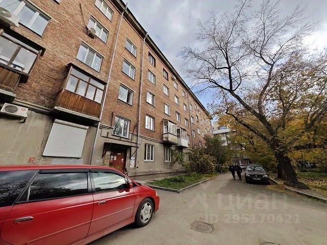 Здание выполнено в советском архитектурном стиле с характерным кирпичным фасадом. На первом этаже расположены окна, а также входная дверь, оформленная в простой, функциональной манере. Балконы на верхних этажах имеют деревянные конструкции, что добавляет теплоты общему виду. Окна большие, что обеспечивает хорошее естественное освещение. Цветовая гамма фасада включает красные и серые оттенки, придающие зданию классический и солидный вид. Внешние стены выглядят ухоженно, хотя на некоторых участках видны следы времени. Общее впечатление создает атмосферу спокойствия и стабильности.