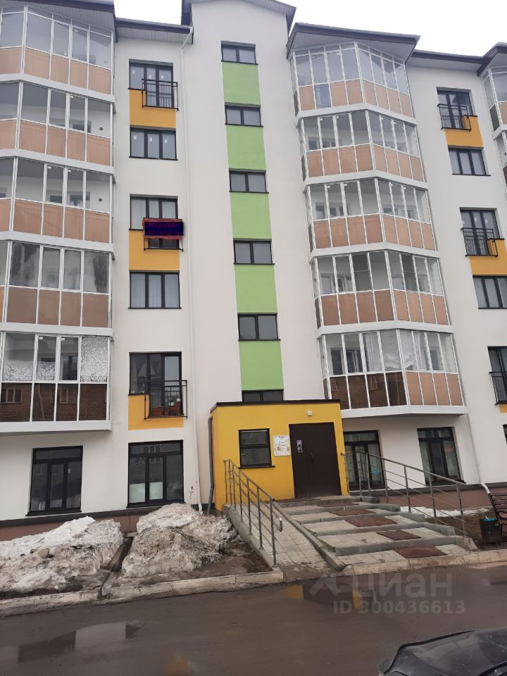 Здание выполнено в современном архитектурном стиле с элементами минимализма. Фасад окрашен в светлые и яркие цвета, включая зеленый и желтый, что придает ему свежий вид. Видны большие окна, обеспечивающие естественное освещение, и балконы с стеклянными перилами. На первом этаже расположена входная группа с удобным пандусом. Ступени и тротуар выложены плиткой, что создает аккуратный и современный облик. Общая структура здания отличается симметрией и четкими линиями, что делает его привлекательным для жителей и гостей.