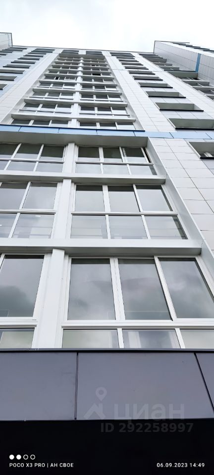 Здание выполнено в современном архитектурном стиле с использованием больших окон, что создает ощущение простора и света. Фасад облицован светлыми панелями, придающими ему стильный и минималистичный вид. Видимые структурные элементы включают вертикальные и горизонтальные линии, которые подчеркивают высоту здания. Окна имеют современный дизайн с тонкими рамами, что усиливает эффект открытости. Цветовая палитра включает светлые тона с акцентами на темные панели внизу, создавая контраст и визуальную гармонию. Общий вид здания отражает современную эстетику и функциональность.