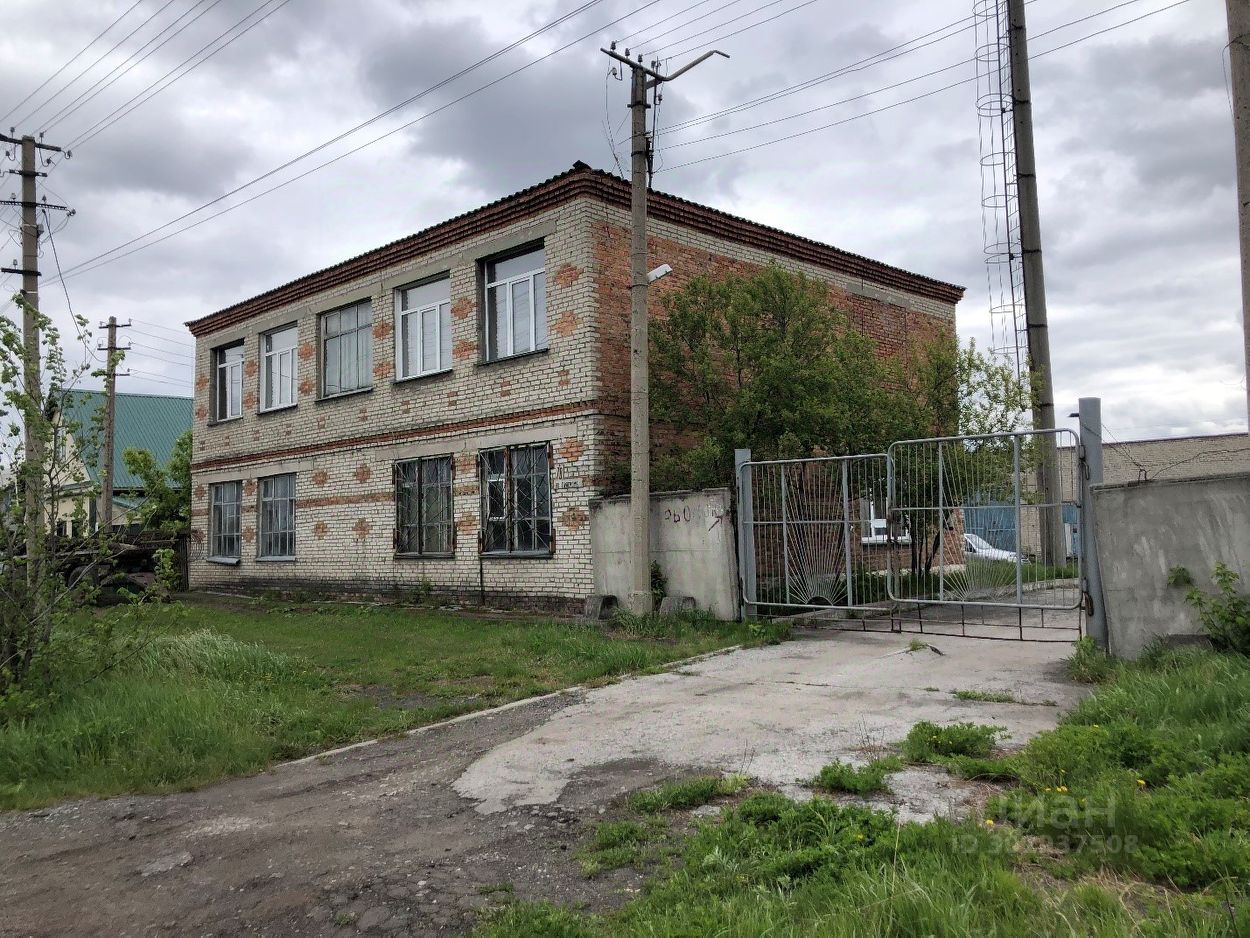 Здание выполнено в простом архитектурном стиле с кирпичной отделкой, на фасаде видны следы времени. Окна большие, с простыми рамами, некоторые из которых повреждены. Структура двухэтажная, с симметричным расположением окон. Входная группа обозначена калиткой, ведущей на небольшую территорию. Основные материалы: кирпич и бетон, что придаёт зданию прочность. Цветовая гамма нейтральная, с преобладанием светлых и кирпичных оттенков. Общее состояние здания требует внимания, что видно по внешнему виду и растительности вокруг.