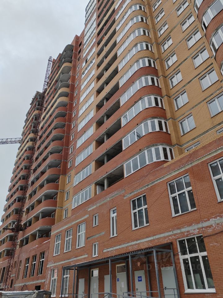 Архитектурный стиль здания представлен современными элементами с плавными линиями и большими окнами. Структурные особенности включают многоэтажную конструкцию с балконами и фасадом из кирпича. Видна нижняя часть здания с входной группой, где расположены окна и двери, обеспечивающие доступ. Основные характеристики включают использование красного кирпича и светлых оконных рам, что создает контраст. Цветовая палитра сочетает теплые и нейтральные тона, а отделка выполнена с акцентом на функциональность и современный дизайн.