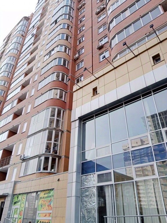 Современное здание в стиле хай-тек с выразительными архитектурными элементами. Фасад выполнен из кирпича и стекла, с округлыми балконами, что придаёт динамичность. На первом этаже большие витрины, обеспечивающие естественное освещение и видимость внутреннего пространства. Использованы светлые и тёмные оттенки, создающие контраст. Основные материалы – кирпич, стекло и металл. Пространство выглядит функционально и стильно, привлекая внимание к современному дизайну. Архитектурные линии плавные, что добавляет эстетики и современности общему виду здания.