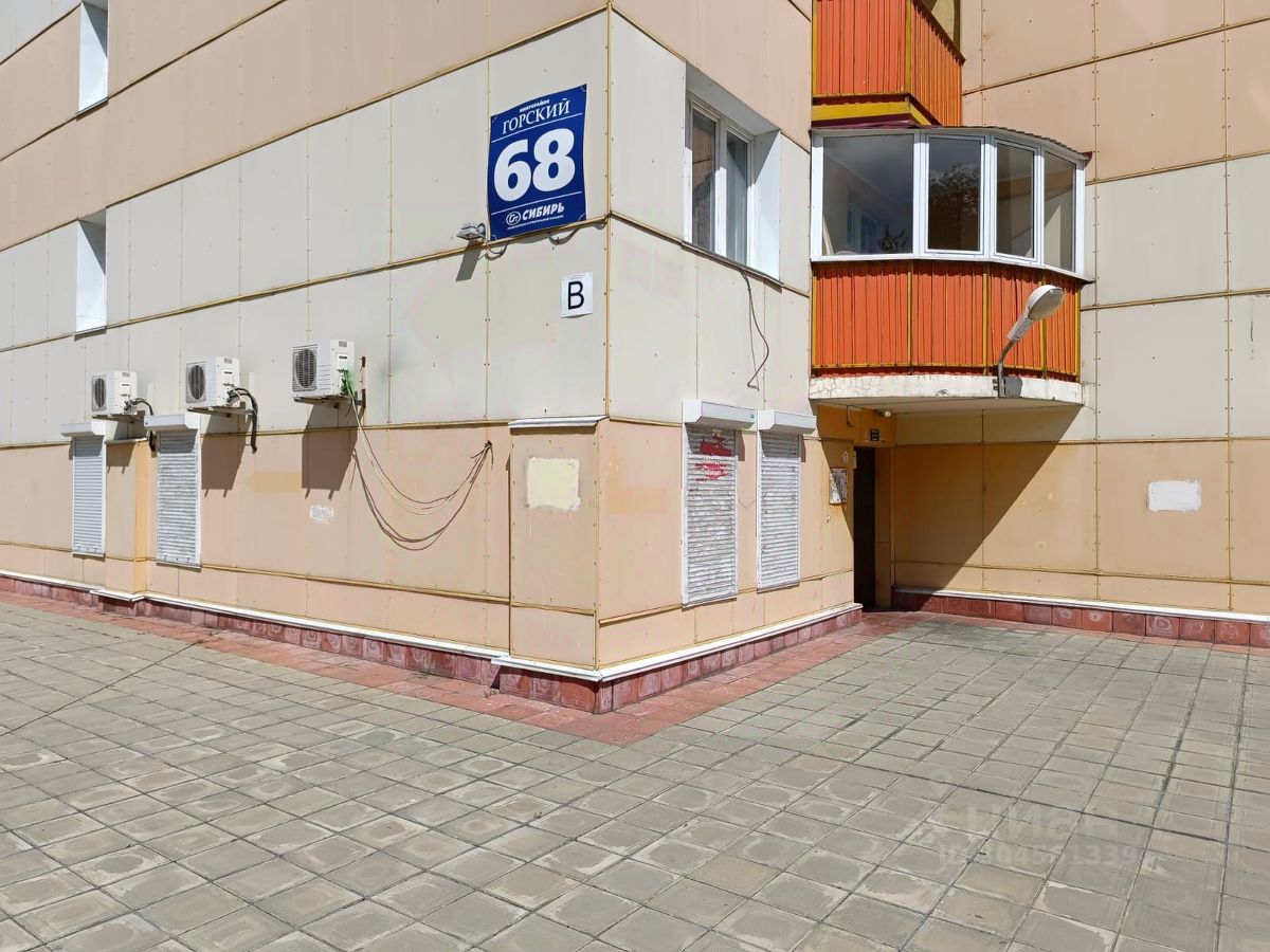 Фасад здания выполнен в современном стиле с элементами минимализма. Стены облицованы панелями светлого цвета, сочетая гладкие и текстурированные поверхности. Видно несколько кондиционеров, расположенных на стене, что подчеркивает функциональность пространства. Объёмный балкон с округлыми окнами выделяется яркой оранжевой отделкой, создавая интересный контраст. Пол выложен плиткой, что придаёт площади современный вид. Входная дверь ведет в зону, которая может быть общим пространством для жильцов. Общая эстетика здания выглядит аккуратно и современно.