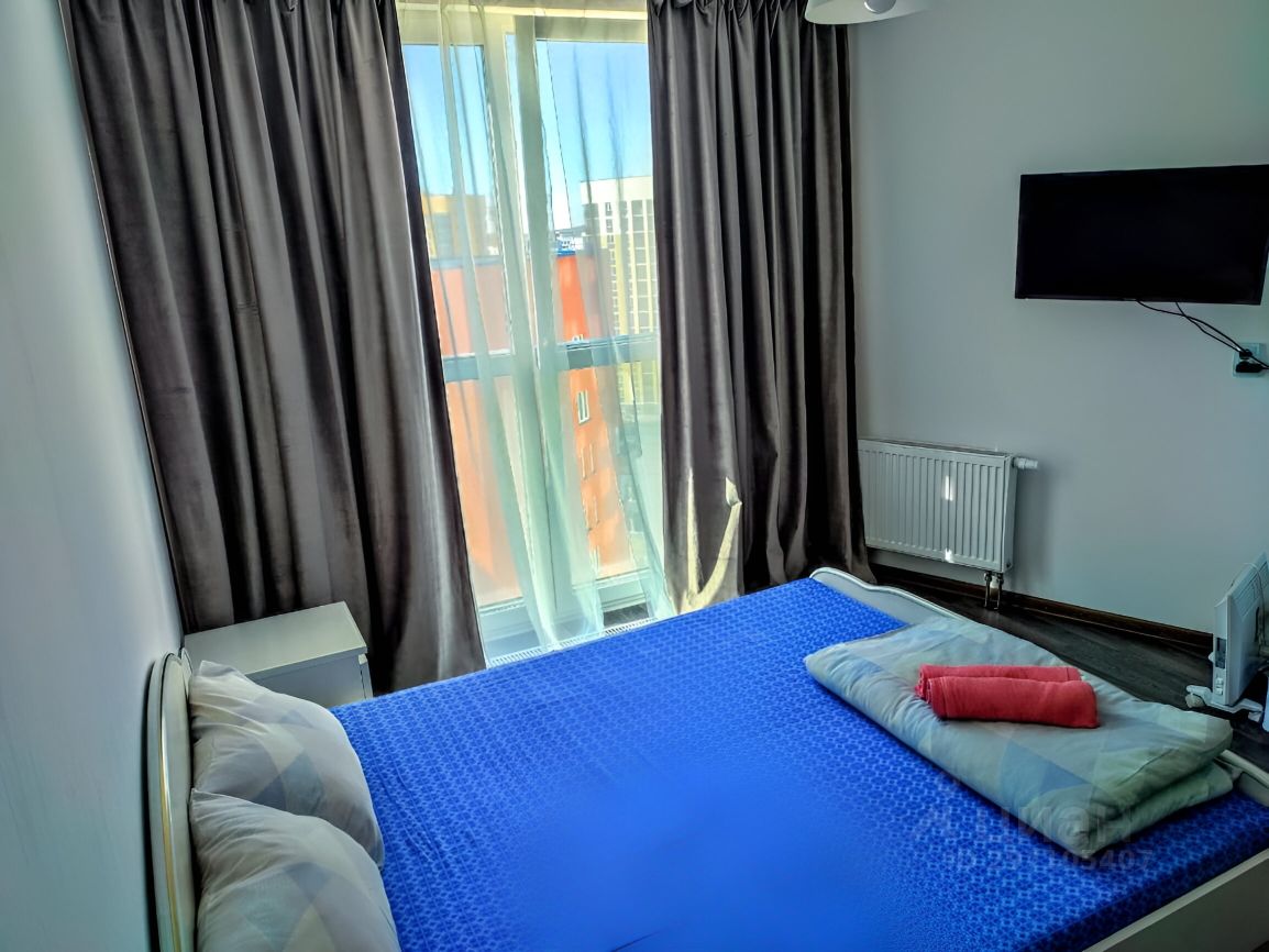 Светлая квартира на 12 этаже в Екатеринбурге. Уютная спальня с большим окном и телевизором. Идеально для краткосрочной аренды.