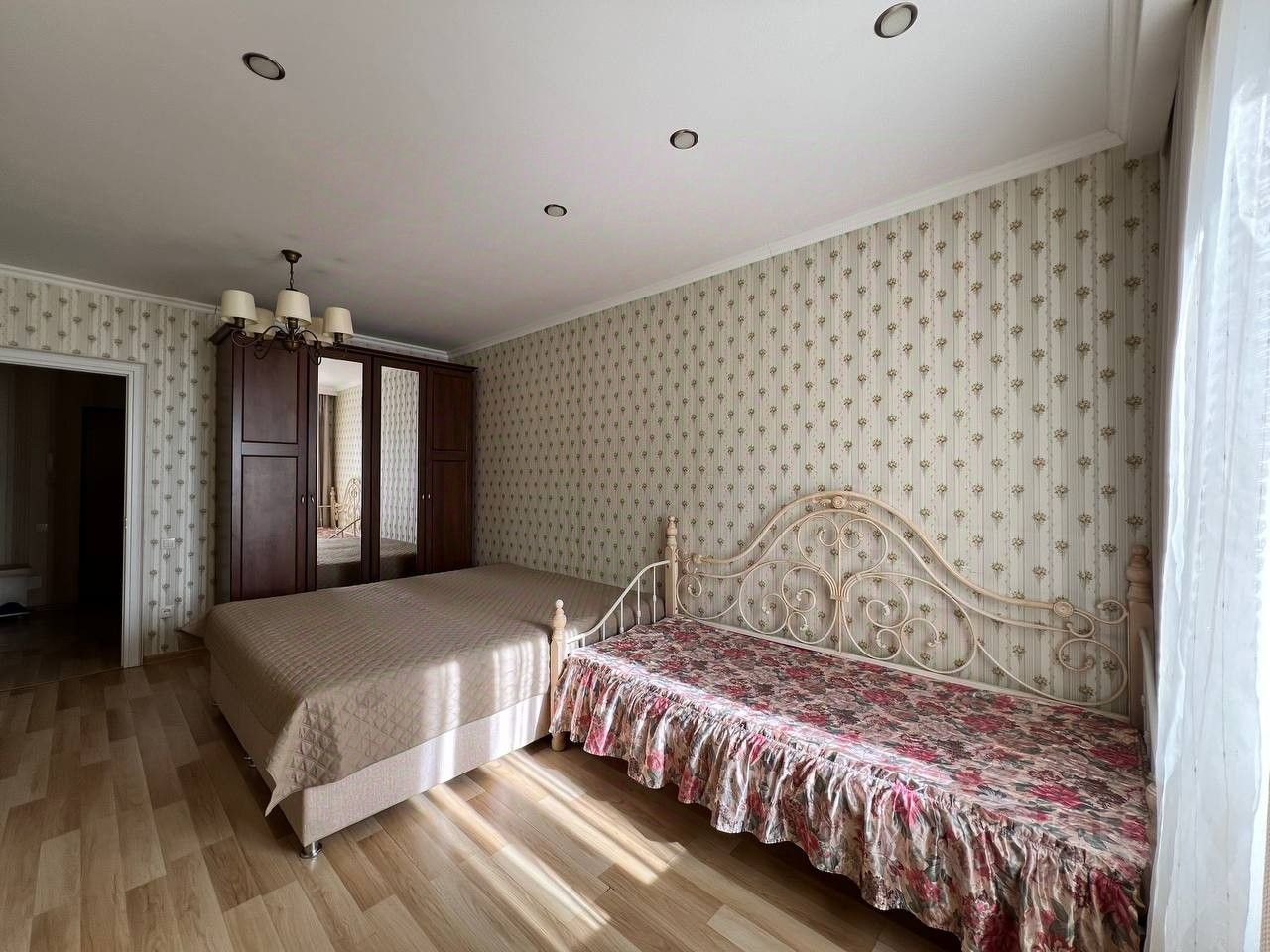 Уютная спальня с двумя кроватями, шкафом и светлыми обоями. Просторная комната с большим окном на 14 этаже в центре Екатеринбурга.