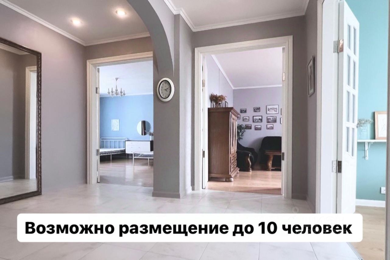 В интерьере заметны современные архитектурные элементы, включая арочные проемы и светлую отделку стен. Пол выполнен из плитки, что создает ощущение простора. Визуально выделяется зона с мебелью, включая диван и деревянный шкаф, а также элементы декора, такие как фотографии на стенах. Цветовая палитра включает серые и голубые оттенки, что придает помещению уют и стиль. Освещение представлено потолочными светильниками и люстрой, создающими мягкий свет. Пространство выглядит функционально и комфортно для проживания.