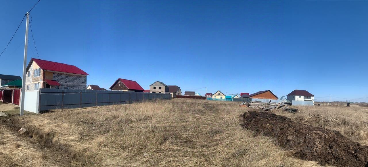 Показаны дома с разнообразными архитектурными стилями, включая здания с красными крышами и каменными стенами. Структуры имеют различные формы и размеры, с забором, ограждающим участок. Видно, что дома расположены на открытой местности, с участками земли, которые могут быть использованы для садоводства или строительства. Основные материалы - кирпич и металл, а цветовая палитра включает красный, белый и светло-зеленый. Завершения зданий простые, но функциональные, что подчеркивает их практичность и доступность для проживания.