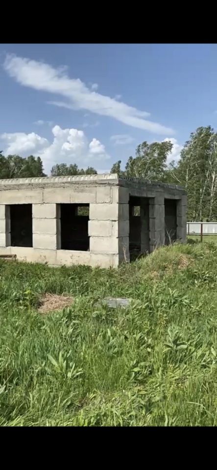 Здание выполнено в простом архитектурном стиле с использованием бетонных блоков. Структурные особенности включают открытые окна и отсутствие крыши, что создает ощущение незавершенности. Видимо, это пространство предназначено для жилого или хозяйственного назначения. Основные характеристики включают прямоугольную форму и четкие линии, что придает зданию современный вид. Материалы представляют собой необработанный бетон, а цветовая палитра нейтральная, с серыми оттенками. Отсутствие отделки подчеркивает сырой, но функциональный характер конструкции.