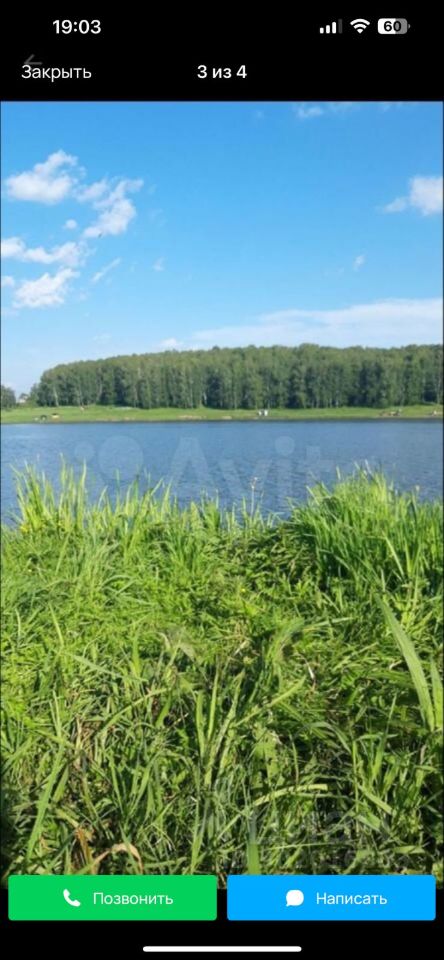 На фотографии виден водоем, окруженный зелеными зарослями травы и кустарников. Вода спокойная, отражает небо с небольшими облаками. На заднем плане виден лес, состоящий из высоких деревьев. Открытое пространство создает ощущение уединения и спокойствия. Цвета природы яркие и насыщенные, преобладают оттенки зеленого и синего. Этот уголок идеально подходит для отдыха на природе или проведения времени на свежем воздухе.