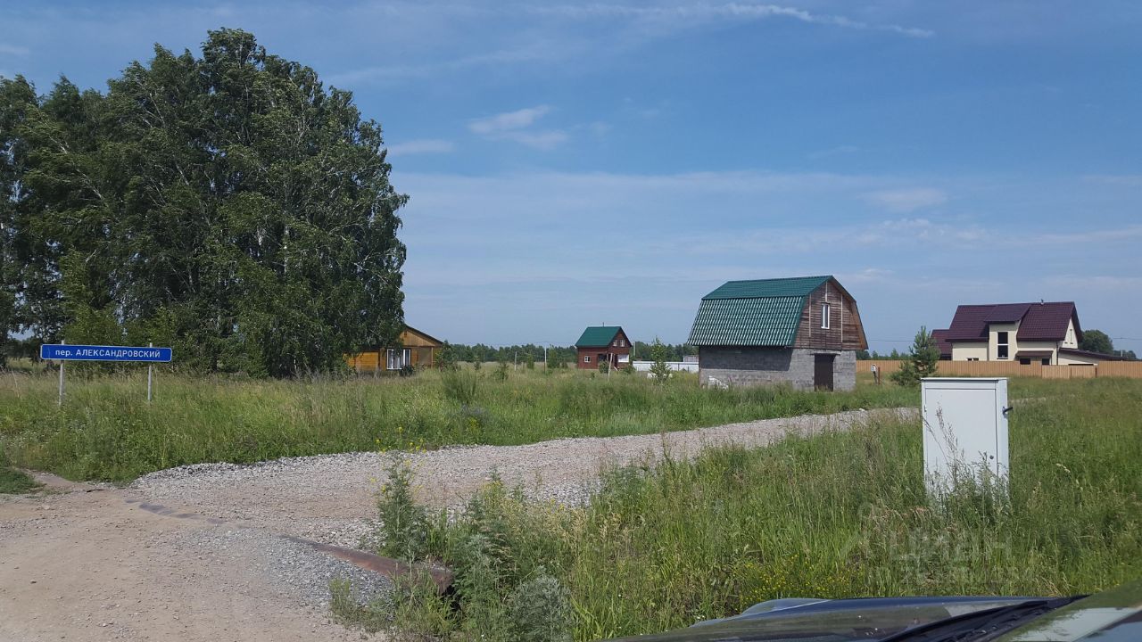 На фотографии видны несколько загородных домов, выполненных в различных архитектурных стилях. Один из домов имеет деревянный фасад с ярко-желтой окраской, другой — с серыми стенами и зеленой крышей. Структурные элементы включают двускатные крыши и большие окна. Видно, что дома расположены на открытой местности с гравийной дорогой. Природные материалы, такие как дерево и камень, доминируют в отделке. Цвета варьируются от теплых желтых до холодных серых и зеленых оттенков, создавая гармоничное сочетание с окружающей природой.