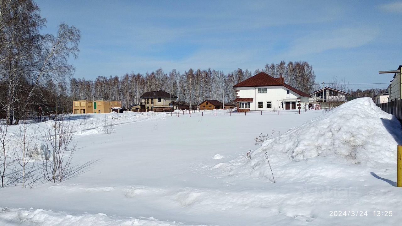 На фотографии виден загородный участок с несколькими домами, выполненными в различных архитектурных стилях. Один из домов отличается классическим дизайном с белыми стенами и красной крышей, а другой имеет более современный вид с деревянной отделкой. Просторная территория покрыта снегом, создавая чистый и спокойный ландшафт. Фасады зданий оформлены большими окнами, что позволяет естественному свету проникать внутрь. Забор вокруг участка выполнен из металлических прутьев, что добавляет уюта и защищенности. В целом, пространство выглядит гармонично и привлекательно для проживания.